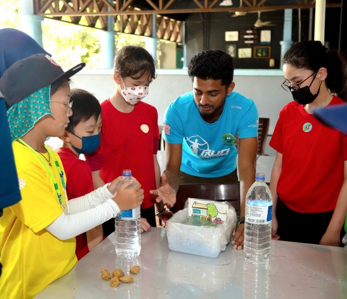 Five children gather round a table with props made of recycled materials including water bottles and other plastic waste